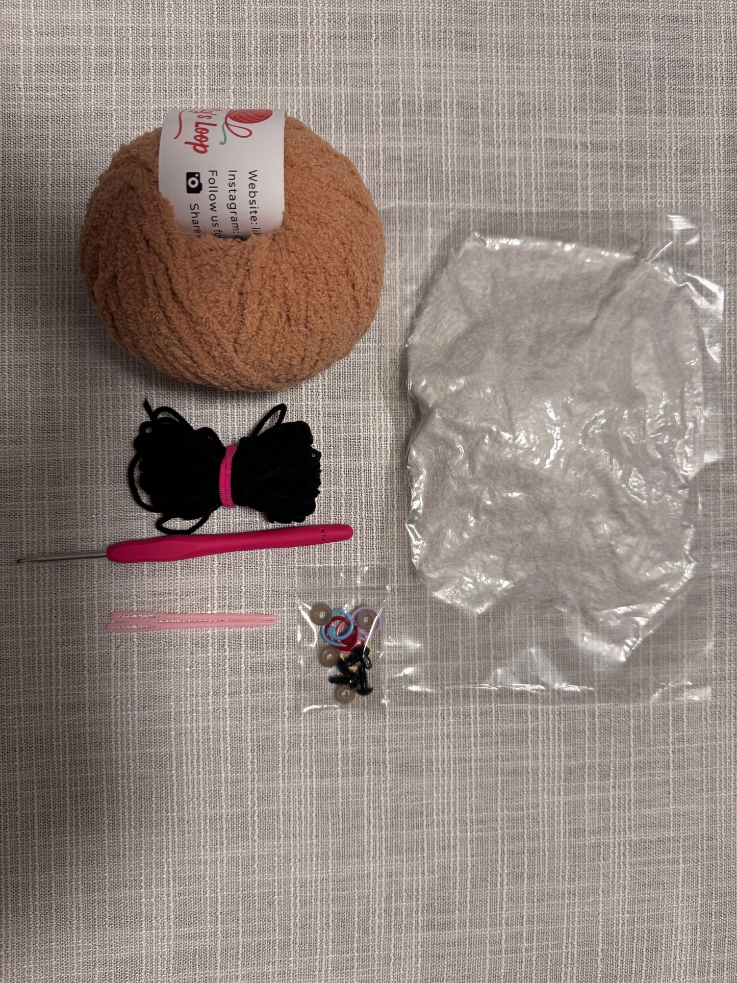 Yarn ball, plastic bag, black yarn, pink crochet hook, and small package on a textured surface