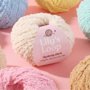Ball of yarn with 'Lily's Loop' label surrounded by other yarn balls on a pink background